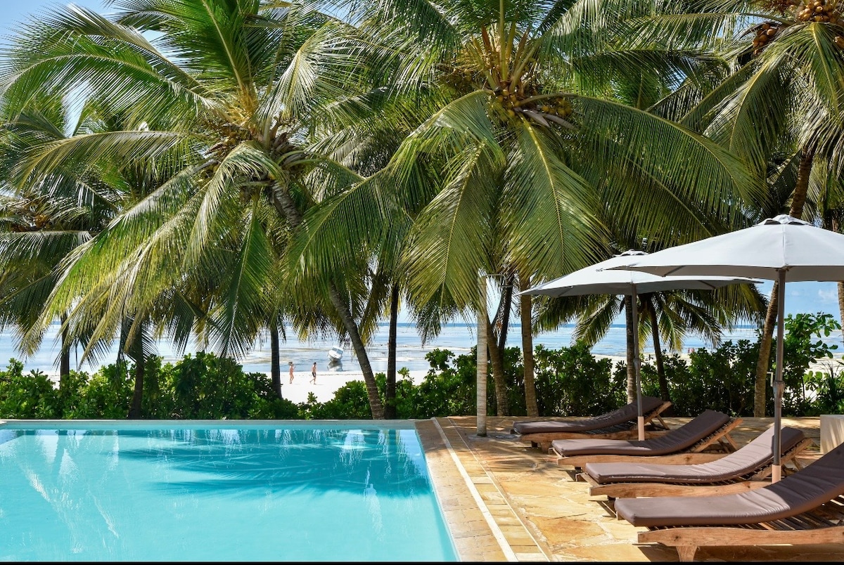 Pool edge with loungers, palms and beach and ocean beyond